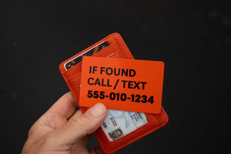 Hand holding an orange Walrus Card in front of a wallet, showing emergency contact information for returning a lost wallet.
